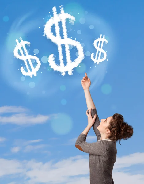 Young girl pointing at dollar sign clouds on blue sky — Stock Photo, Image