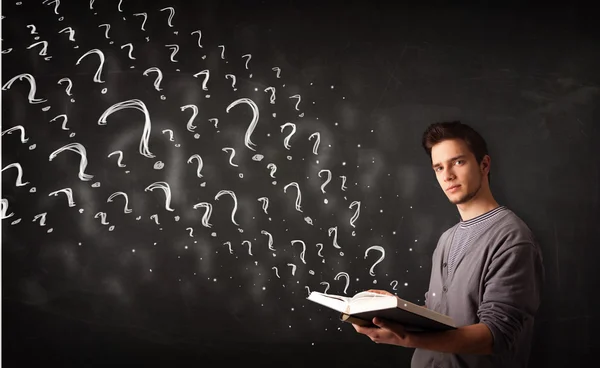 Young man reading a book with question marks coming out from it — Stock Photo, Image