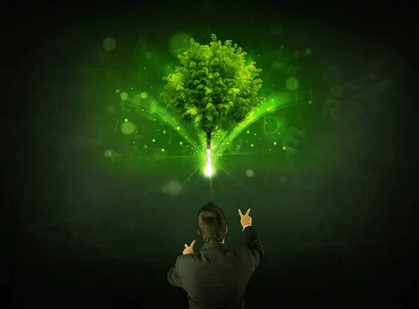 Geschäftsmann gestikuliert vor einem leuchtenden Baum — Stockfoto