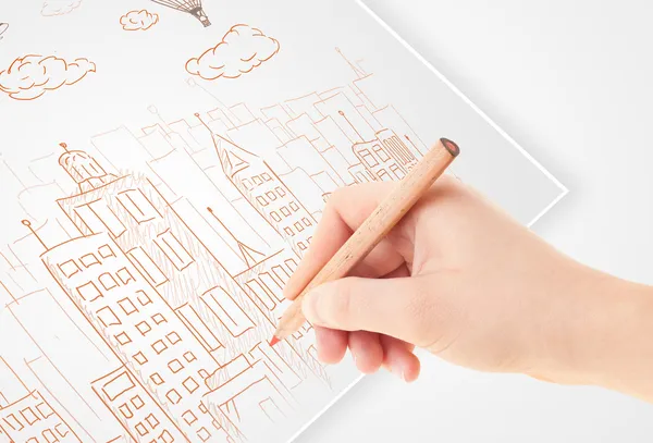 Een persoon die het tekenen van de schets van een stad met ballonnen en wolken op een — Stockfoto