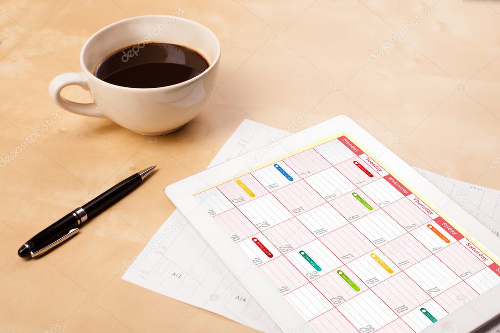 Tablet pc showing calendar on screen with a cup of coffee on a d