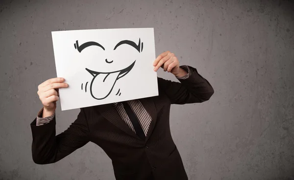 Businessman holding a paper with funny smiley face in front of h — Stock Photo, Image