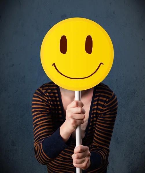 Young woman holding a smiley face emoticon — Stock Photo, Image