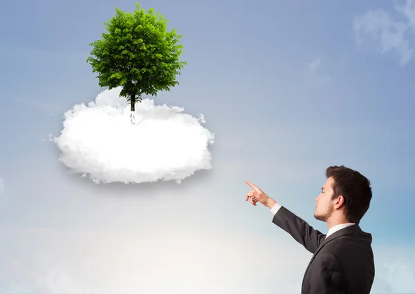 Young man pointing at a green tree on top of a white cloud — Stock Photo, Image