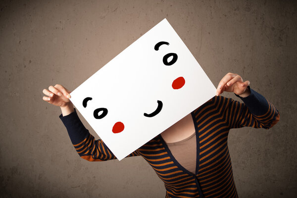 Woman holding a cardboard with a smiley face on it