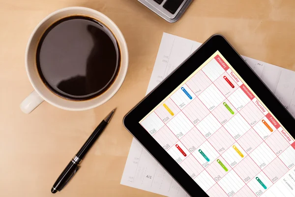 Tablet pc kalendarz wyświetlone na ekranie przy filiżance kawy na d — Zdjęcie stockowe