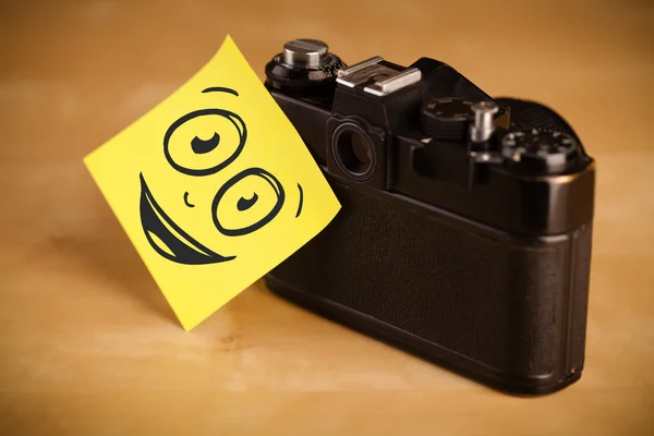 Post-it opmerking met smileygezicht gevezen op fotocamera — Stockfoto