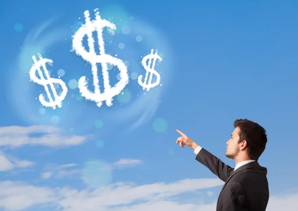 Empresario apuntando a nubes de signo de dólar en el cielo azul — Foto de Stock