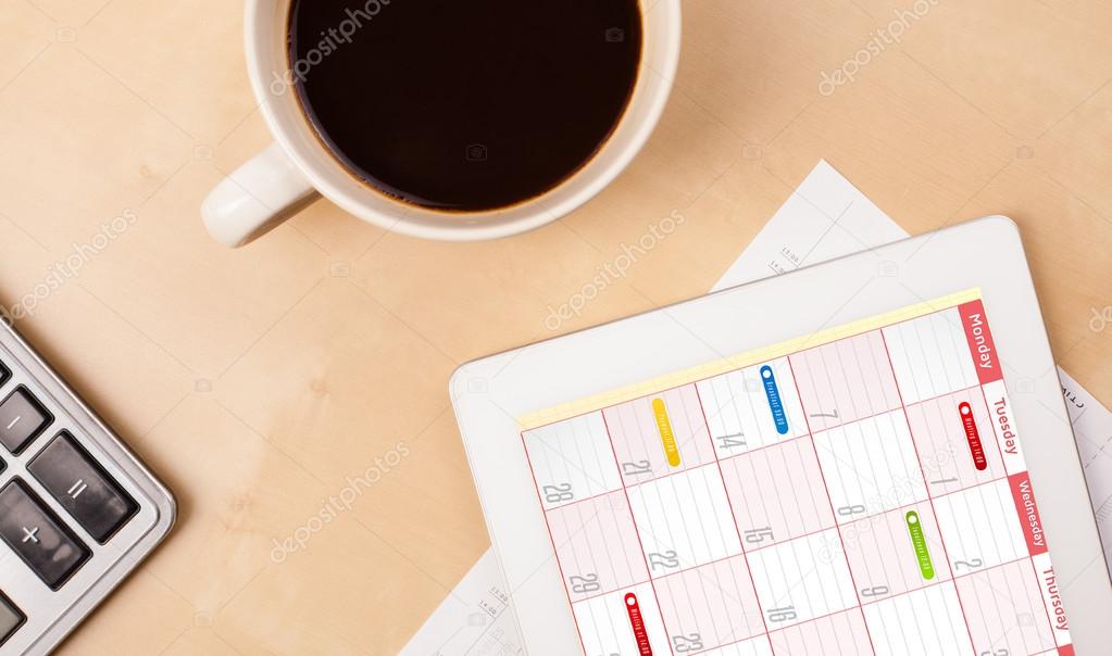 Tablet pc showing calendar on screen with a cup of coffee on a d