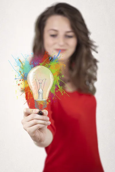 Jovencita dibujando una bombilla de colores con salpicaduras de colores —  Fotos de Stock