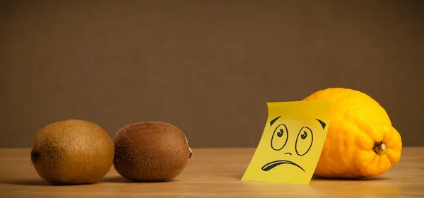Lemon with sticky post-it note looking sadly at kiwis — Stock Photo, Image