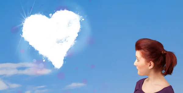 Cute girl looking at white heart cloud on blue sky — Stock Photo, Image