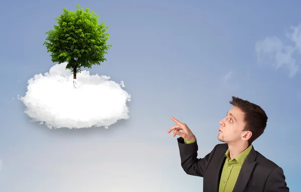 Young man pointing at a green tree on top of a white cloud — Stock Photo, Image