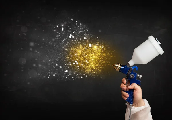 Worker with airbrush painting with glowing golden paint — Stock Photo, Image