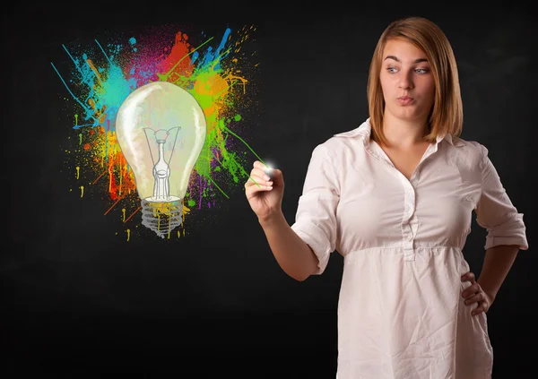 Young lady drawing a colorful light bulb with colorful splashes — Stock Photo, Image