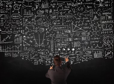 İşadamı tahtaya çizilmiş çizelgelerin önünde duruyor.