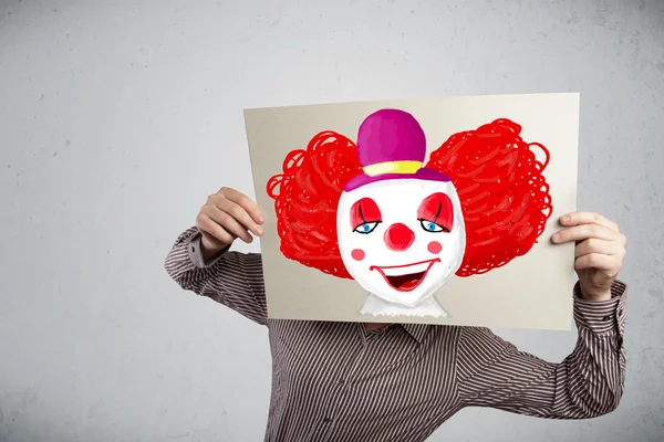 Businessman holding a cardboard with a clown on it in front of h — Stock Photo, Image