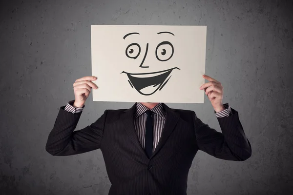 Businessman holding a cardboard with smiley face on it in front — Stock Photo, Image