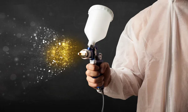 Worker with airbrush painting with glowing golden paint — Stock Photo, Image