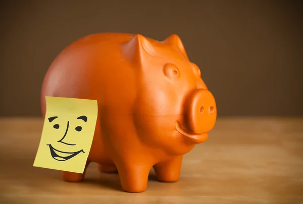 Post-it note with smiley face sticked on piggy bank — Stock Photo, Image