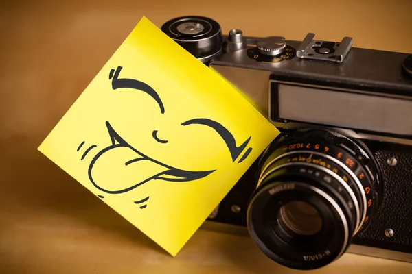 Post-it opmerking met smileygezicht gevezen op fotocamera — Stockfoto