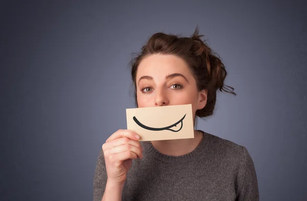 Pretty young girl holding white card with smile drawing — Stock Photo, Image