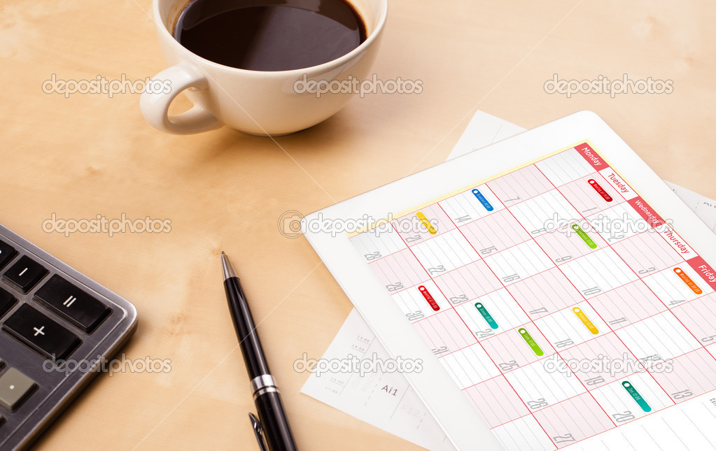 Tablet pc showing calendar on screen with a cup of coffee on a d