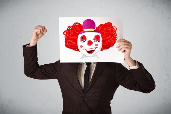 Businessman holding a cardboard with a clown on it in front of h — Stock Photo, Image