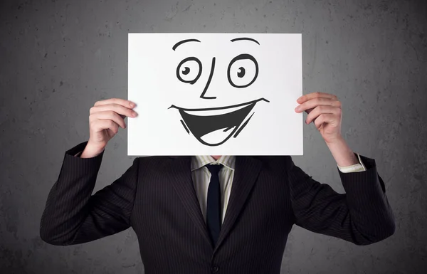 Empresário segurando um papelão com rosto sorridente na frente — Fotografia de Stock