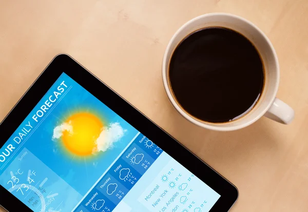 Tablet pc showing weather forecast on screen with a cup of coffe — Stock Photo, Image