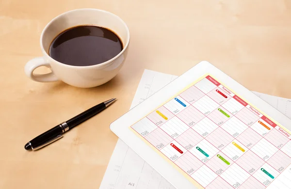 Tablet pc che mostra il calendario sullo schermo con una tazza di caffè su un d — Foto Stock