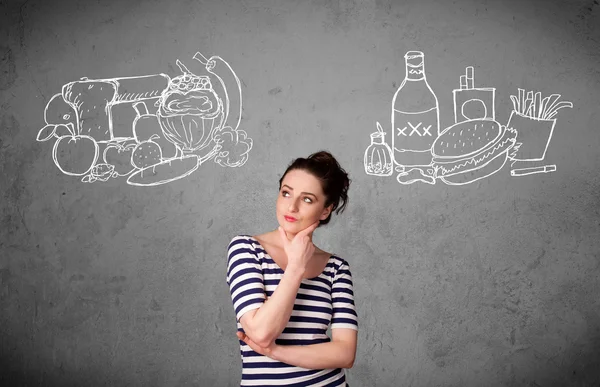 Woman standing between healthy and unhealthy foods — Stock Photo, Image