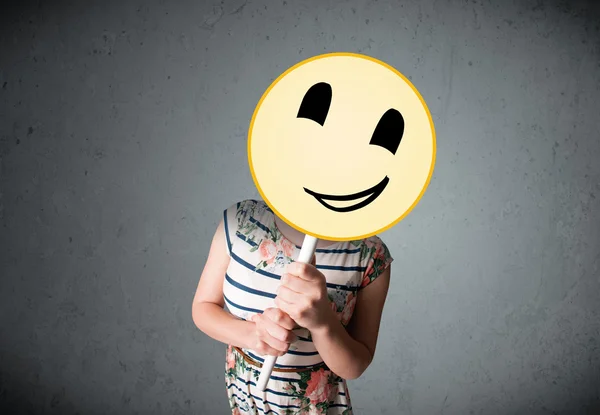 Mujer joven sosteniendo un emoticono sonriente —  Fotos de Stock