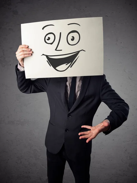 Businessman holding a cardboard with smiley face on it in front — Stock Photo, Image