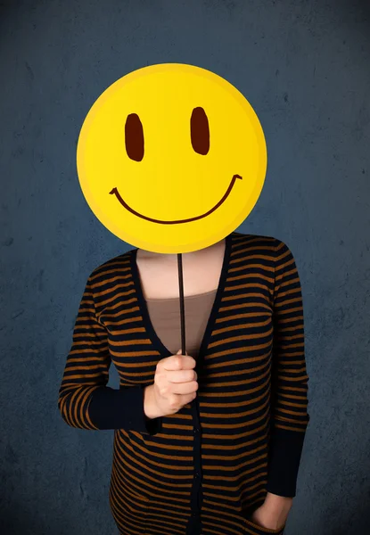 Mujer joven sosteniendo un emoticono sonriente —  Fotos de Stock