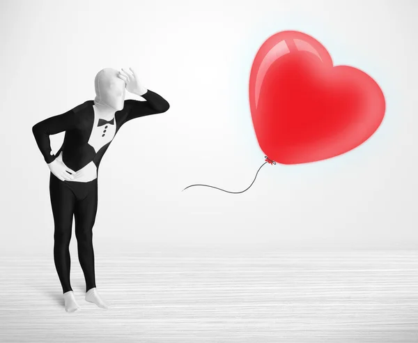 Cute guy in morpsuit body suit looking at a balloon shaped heart — Stock Photo, Image