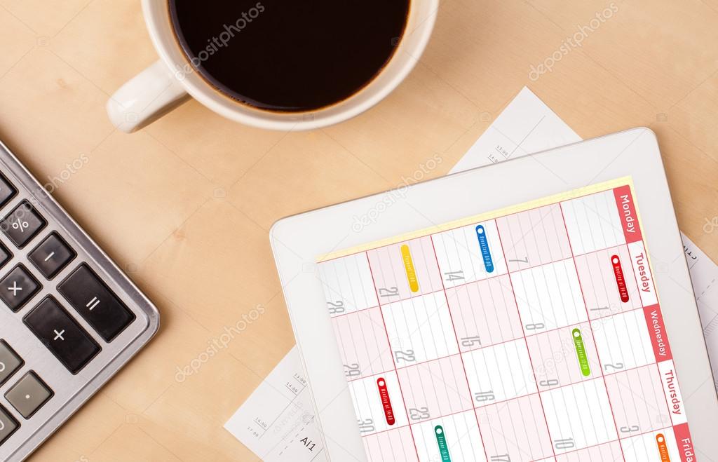 Tablet pc showing calendar on screen with a cup of coffee on a d