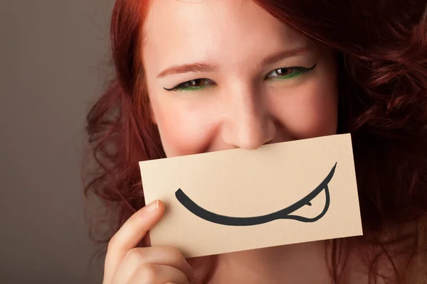 Pretty young girl holding white card with smile drawing — Stock Photo, Image