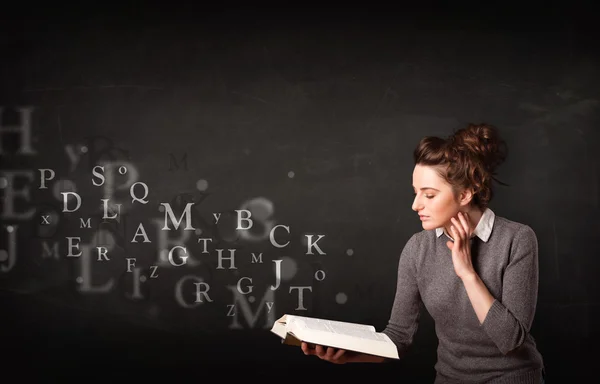 Jovencita leyendo un libro con letras del alfabeto — Foto de Stock