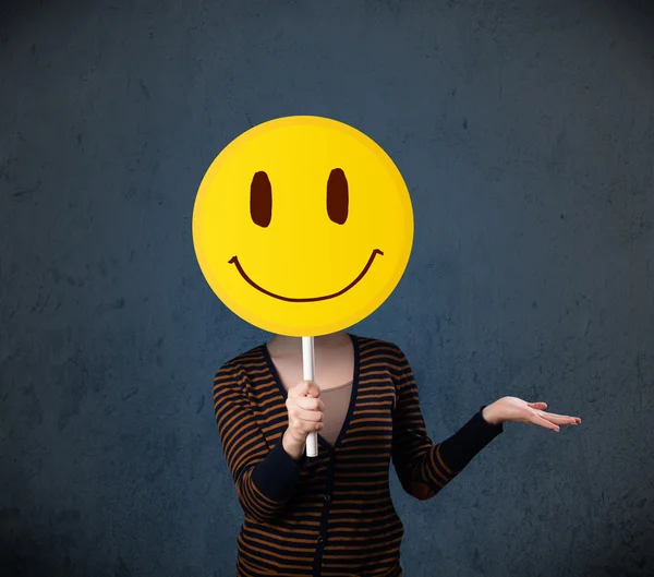 Young woman holding a smiley face emoticon — Stock Photo, Image