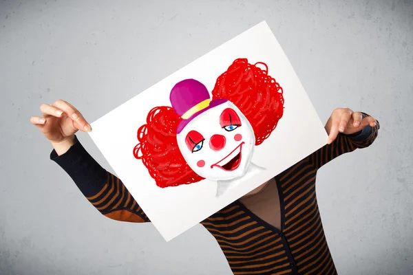 Woman holding a cardboard with a clown on it in front of her hea — Stock Photo, Image
