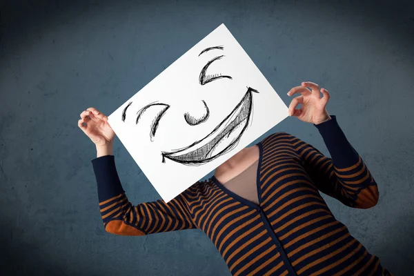 Kobieta z narysowaną uśmiechniętą twarzą na papierze przed głową — Zdjęcie stockowe