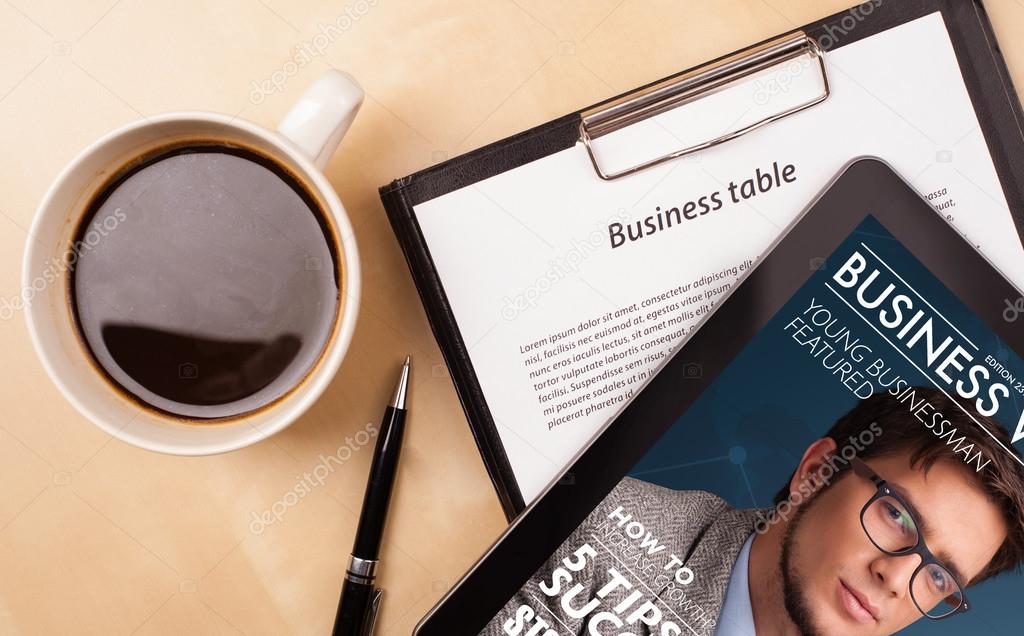 Tablet pc showing magazine on screen with a cup of coffee on a d