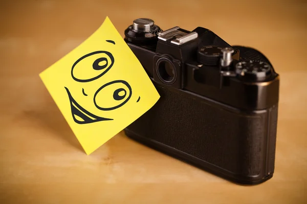 Post-it opmerking met smileygezicht gevezen op fotocamera — Stockfoto