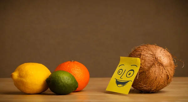 Coconut with post-it note smiling at citrus fruits — Stock Photo, Image