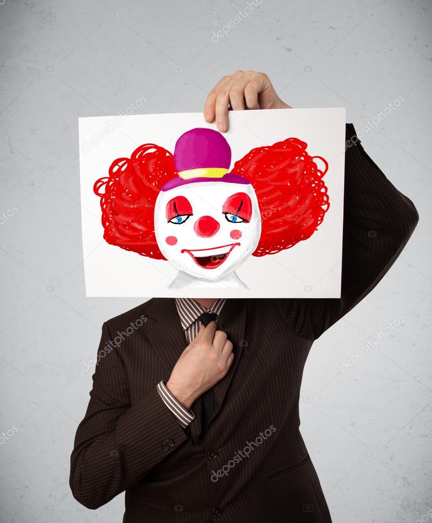 Businessman holding a cardboard with a clown on it in front of h