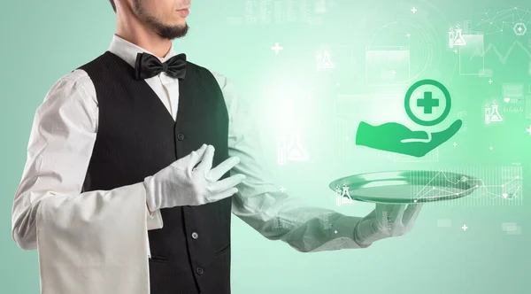 Handsome young waiter in tuxedo holding healthcare icons on tray — Stock Photo, Image