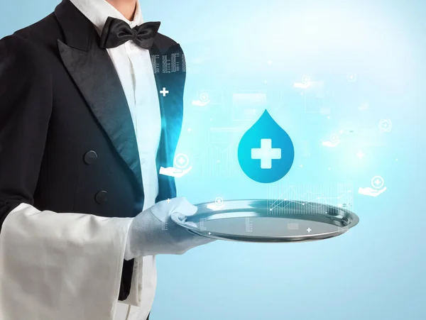 Handsome young waiter in tuxedo holding healthcare icons on tray — Stock Photo, Image