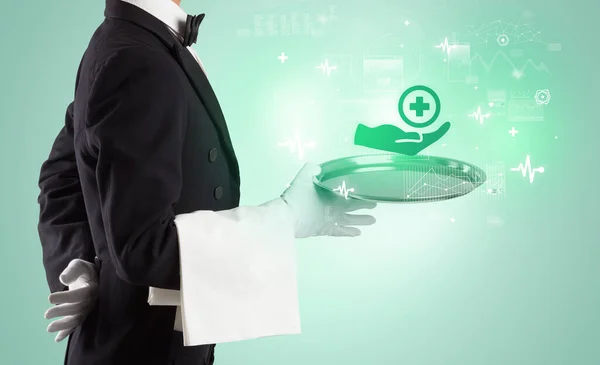 Handsome young waiter in tuxedo holding healthcare icons on tray — Stock Photo, Image