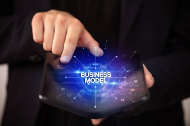 İş adamı, üzerinde iş modeli yazıları ve yeni iş konsepti olan katlanabilir bir akıllı telefon tutuyor.